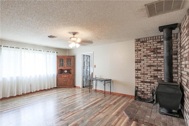 living area featuring a wood stove, visible vents, a ceiling fan, and wood finished floors