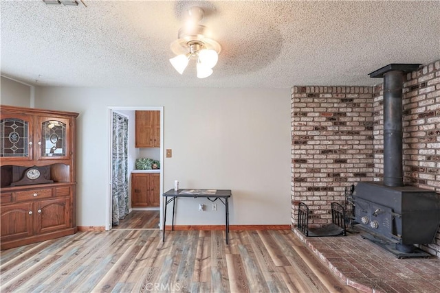 interior space with a wood stove, light wood-style flooring, a textured ceiling, a ceiling fan, and visible vents