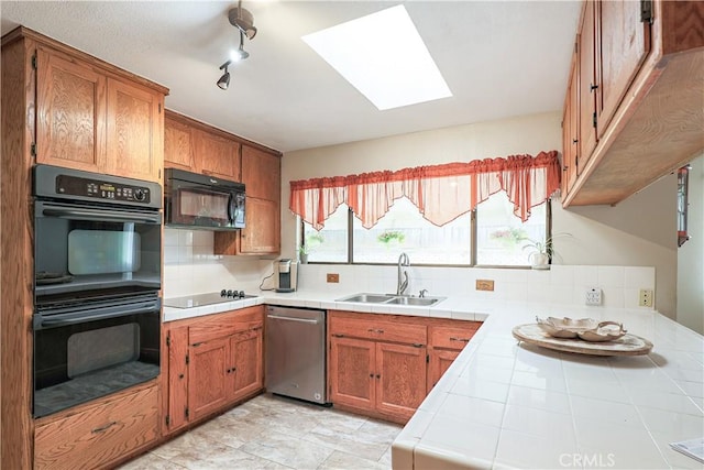 kitchen featuring a sink, brown cabinets, black appliances, a skylight, and tile countertops