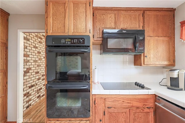 kitchen with tasteful backsplash, tile counters, black appliances, and brown cabinets