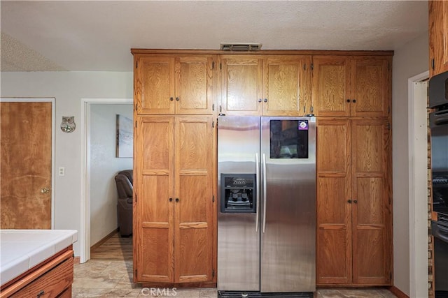 kitchen with brown cabinetry, visible vents, black oven, stainless steel fridge, and tile counters