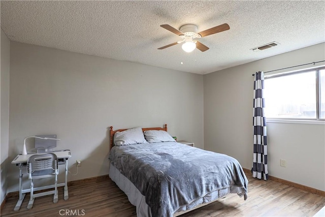 bedroom with visible vents, a textured ceiling, a ceiling fan, and wood finished floors
