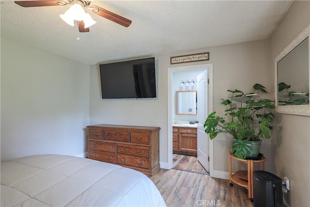 bedroom with a textured ceiling, a sink, ensuite bathroom, ceiling fan, and light wood-style flooring