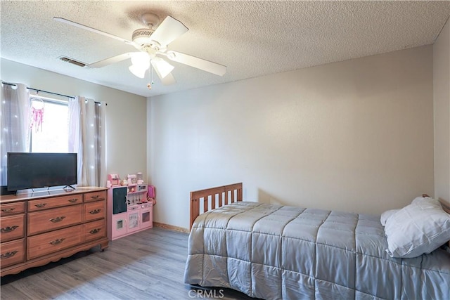 bedroom featuring light wood-style flooring, a textured ceiling, ceiling fan, and visible vents