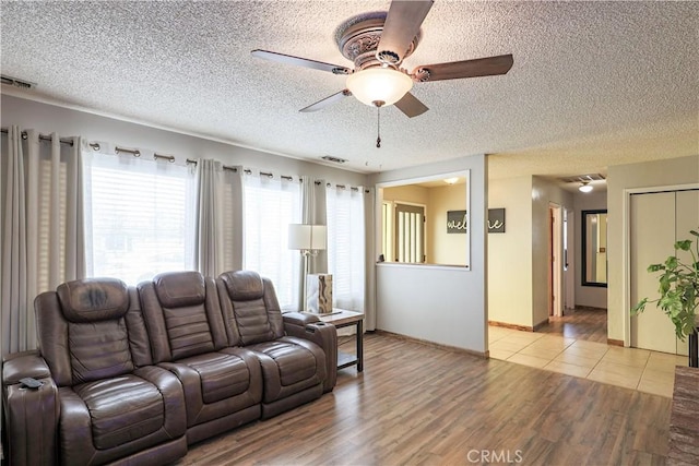 living area with light wood finished floors, visible vents, a textured ceiling, and ceiling fan