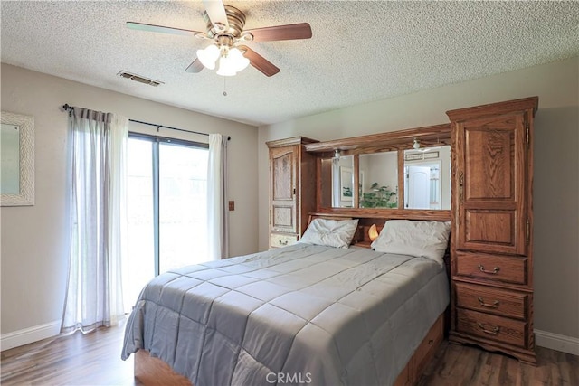 bedroom with visible vents, a textured ceiling, baseboards, and wood finished floors