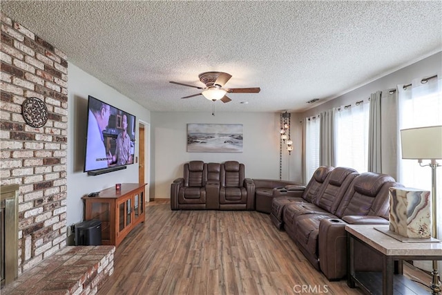 living area with baseboards, a fireplace, a textured ceiling, a ceiling fan, and wood-type flooring