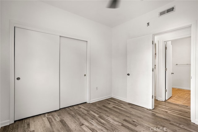 unfurnished bedroom featuring wood finished floors, a closet, and visible vents