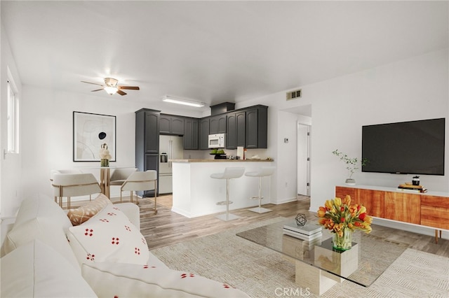 living room with light wood-style flooring, ceiling fan, and visible vents