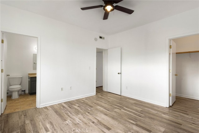 unfurnished bedroom featuring visible vents, baseboards, a spacious closet, light wood finished floors, and ensuite bath
