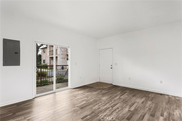 spare room featuring electric panel, baseboards, and wood finished floors