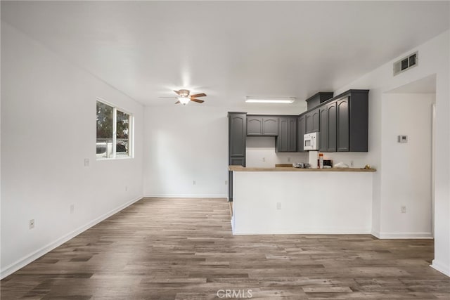 kitchen featuring visible vents, ceiling fan, a peninsula, white microwave, and wood finished floors