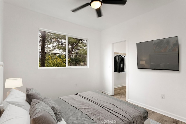 bedroom with a closet, baseboards, a ceiling fan, a walk in closet, and wood finished floors