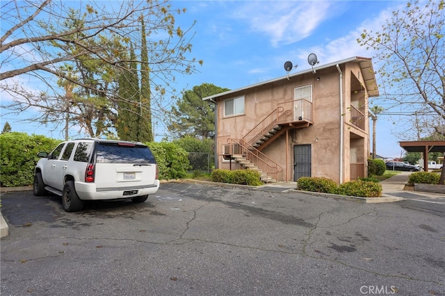 exterior space with stairs, stucco siding, and uncovered parking