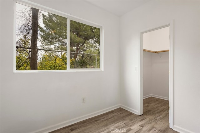 unfurnished bedroom featuring wood finished floors, a closet, baseboards, and a spacious closet
