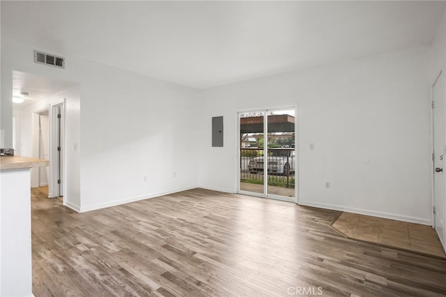 empty room with electric panel, visible vents, baseboards, and wood finished floors
