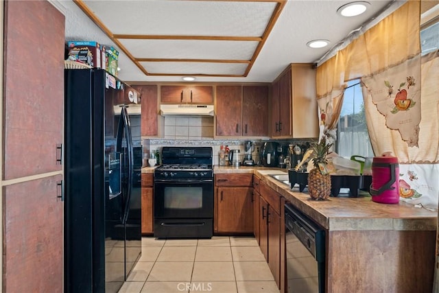 kitchen with black appliances, under cabinet range hood, light tile patterned floors, brown cabinetry, and decorative backsplash