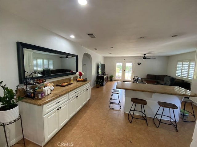 kitchen with open floor plan, a breakfast bar, arched walkways, white cabinets, and visible vents