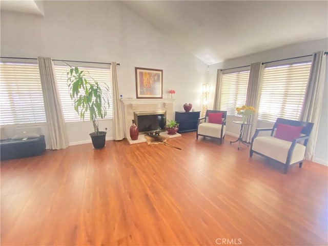 sitting room with high vaulted ceiling, baseboards, a glass covered fireplace, and wood finished floors