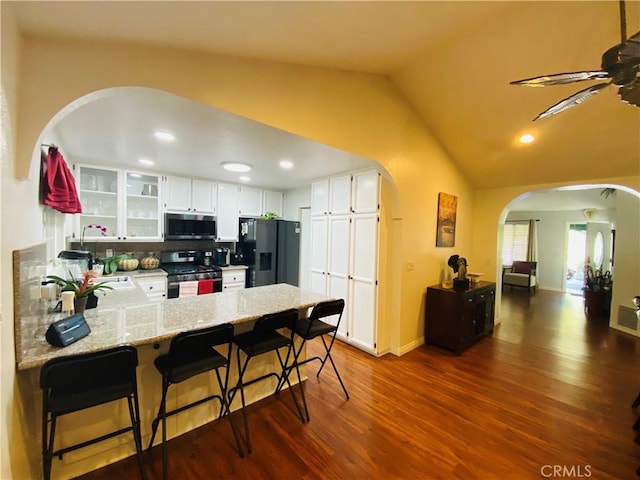 kitchen with a peninsula, arched walkways, appliances with stainless steel finishes, and dark wood-type flooring