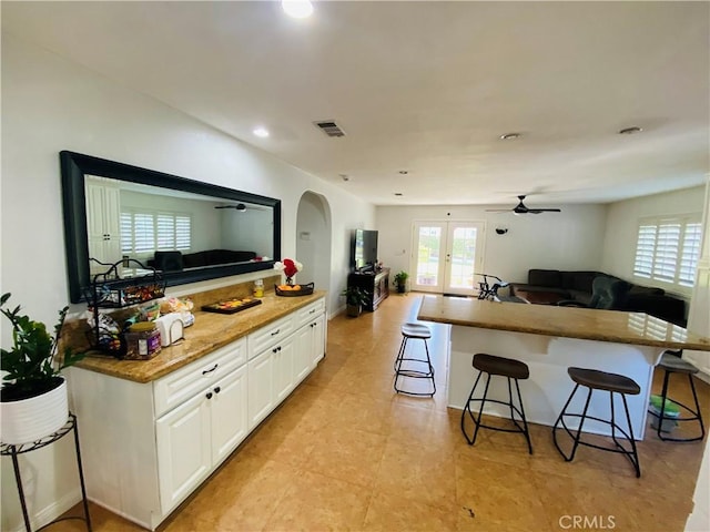 kitchen with open floor plan, arched walkways, a kitchen bar, white cabinets, and visible vents