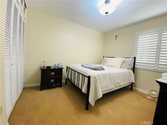 bedroom with baseboards, a closet, and light colored carpet