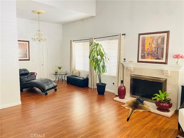 living area featuring a fireplace, wood finished floors, baseboards, and an inviting chandelier
