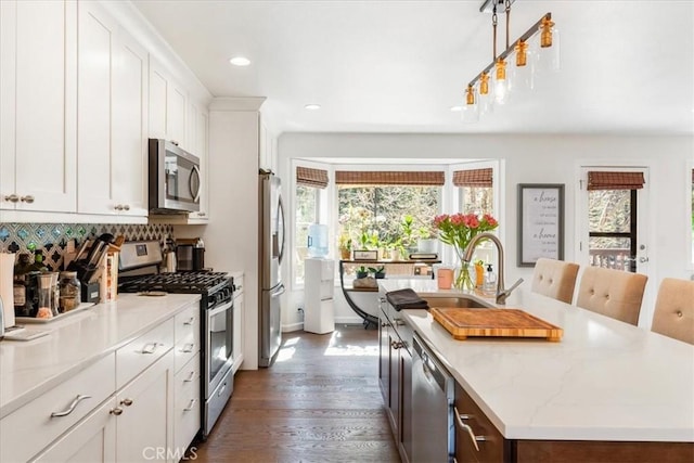 kitchen with stainless steel appliances, a wealth of natural light, an island with sink, and a sink