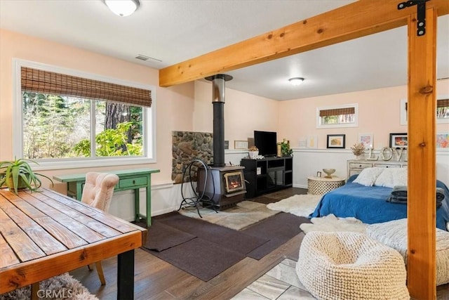 bedroom featuring visible vents, a wood stove, wood finished floors, and beamed ceiling