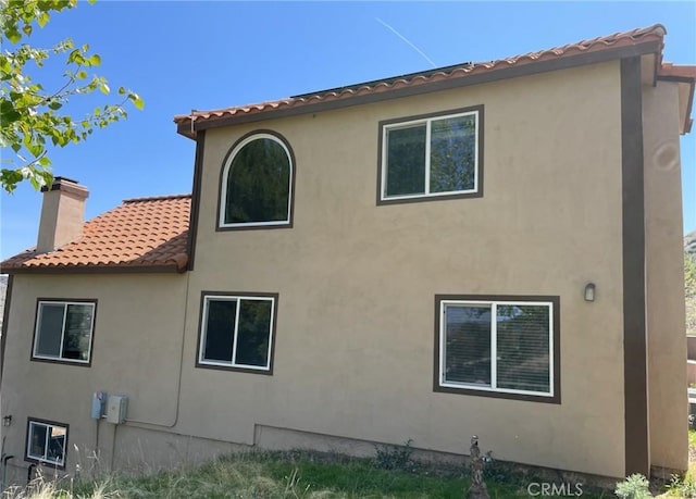 view of side of home with a tile roof, stucco siding, and a chimney