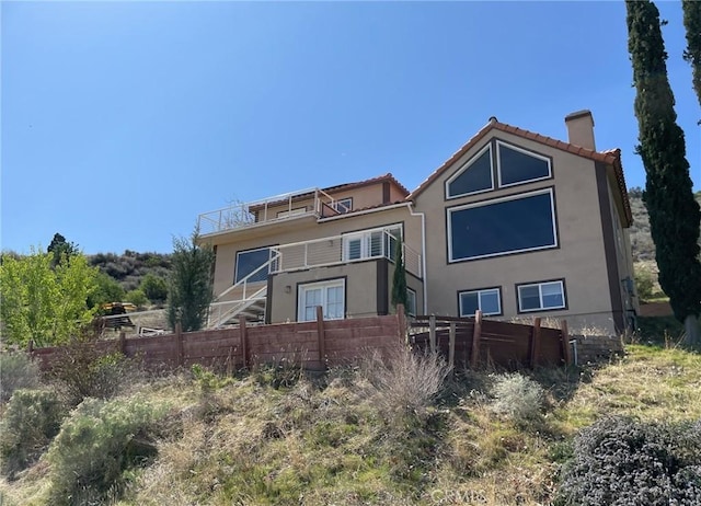back of property with stucco siding, fence, a tile roof, a balcony, and a chimney