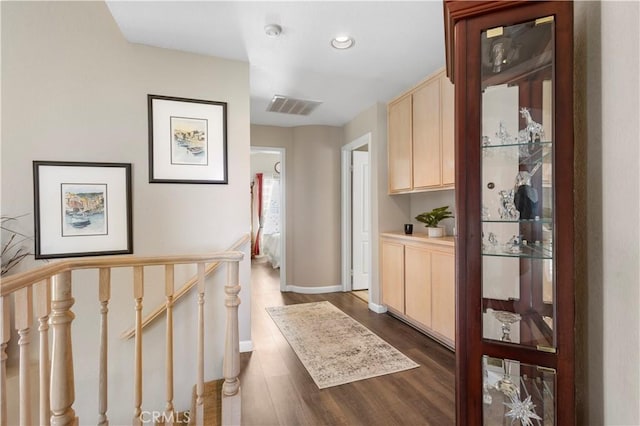 hall with an upstairs landing, dark wood-style flooring, baseboards, and visible vents