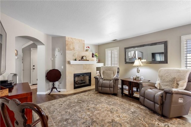 living room featuring baseboards, arched walkways, a textured ceiling, a fireplace, and wood finished floors