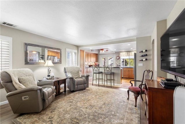 living area featuring light wood-style floors, ceiling fan, a textured ceiling, visible vents, and baseboards