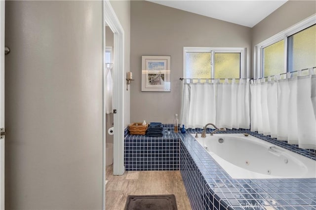 full bathroom with wood finished floors, a tub with jets, and vaulted ceiling