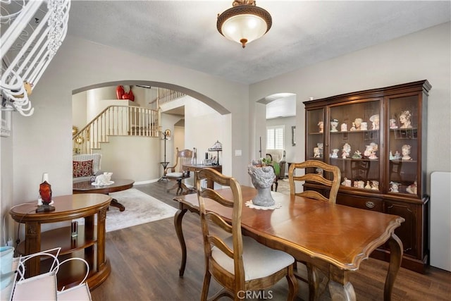 dining area with arched walkways, dark wood finished floors, a textured ceiling, and stairs