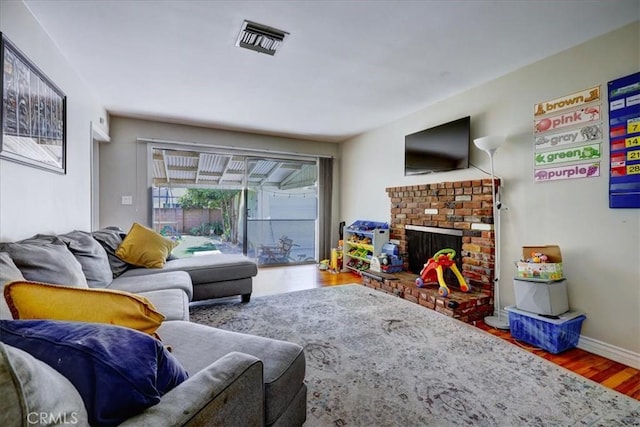 living area with a brick fireplace, visible vents, baseboards, and wood finished floors