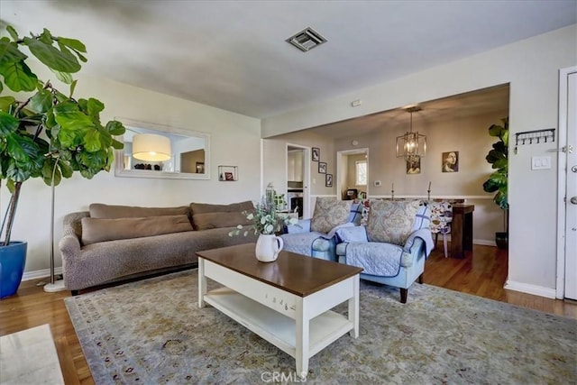 living area with a chandelier, wood finished floors, baseboards, and visible vents