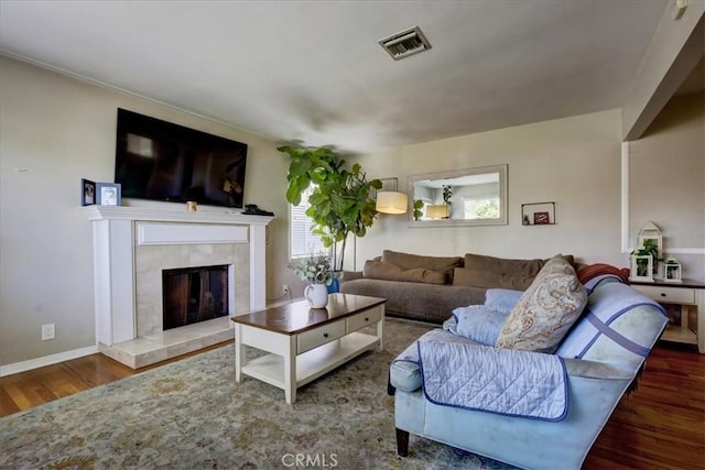 living area with baseboards, wood finished floors, a tiled fireplace, and visible vents