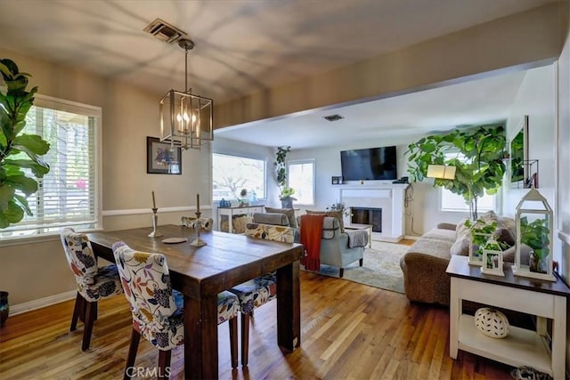dining space with visible vents, a glass covered fireplace, a notable chandelier, and light wood-style floors