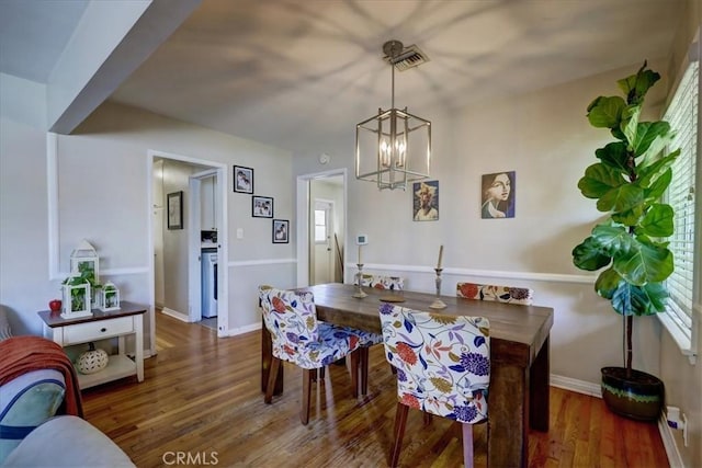 dining space with wood finished floors, visible vents, a notable chandelier, and baseboards