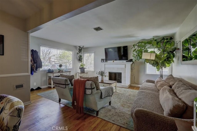 living area featuring a fireplace, visible vents, baseboards, and wood finished floors
