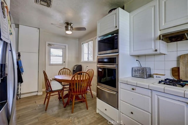 kitchen featuring tile counters, a warming drawer, white cabinets, visible vents, and stainless steel appliances