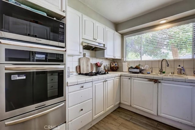 kitchen featuring a sink, under cabinet range hood, white gas cooktop, white cabinetry, and tile countertops