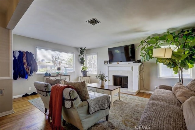 living area with a fireplace, visible vents, baseboards, and wood finished floors