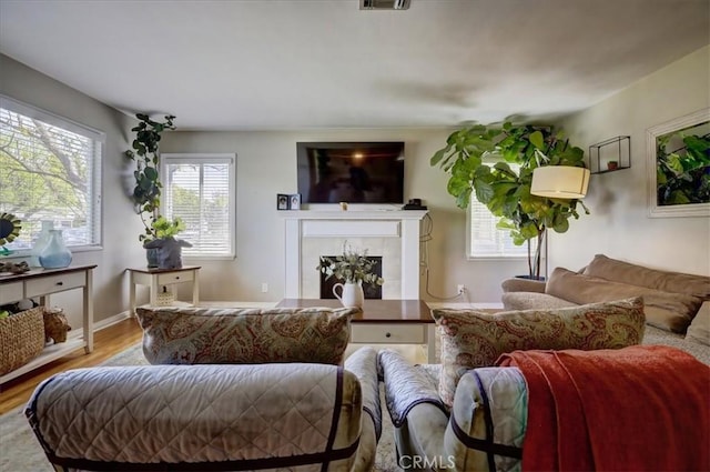 living room featuring a tile fireplace, visible vents, baseboards, and wood finished floors