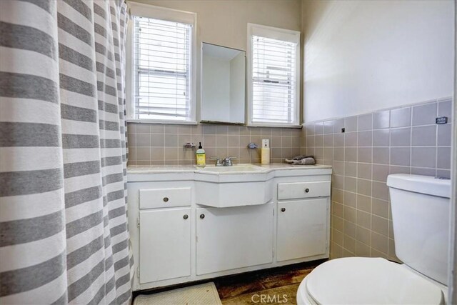 bathroom featuring toilet, wood finished floors, vanity, and tile walls