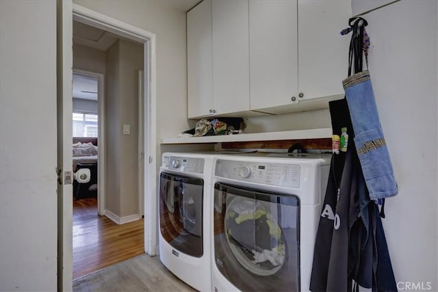 clothes washing area with light wood finished floors, washing machine and clothes dryer, baseboards, and cabinet space