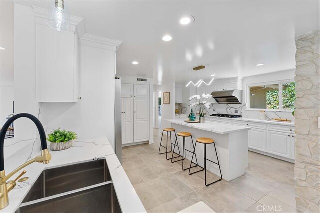 950 S Spring Meadow Dr, West Covina, CA 91791 - kitchen with under cabinet range hood, a sink, white cabinetry, light stone counters, and a kitchen breakfast bar