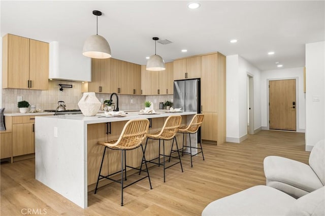 kitchen with light countertops, light brown cabinets, freestanding refrigerator, and tasteful backsplash
